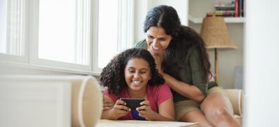 A mother and daughter relaxing together while looking at something on a smartphone.