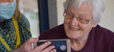 A mother watching Mother's Day messages from family on a phone with help from an adult in a face mask.
