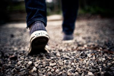 Close up photo of sneaker-clad feet walking away from the camera on gravel. 
