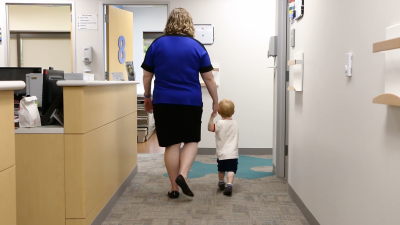 A doctor leads a child into an office to be screened with a Modified Checklist for Autism in Toddler, or M-CHAT.