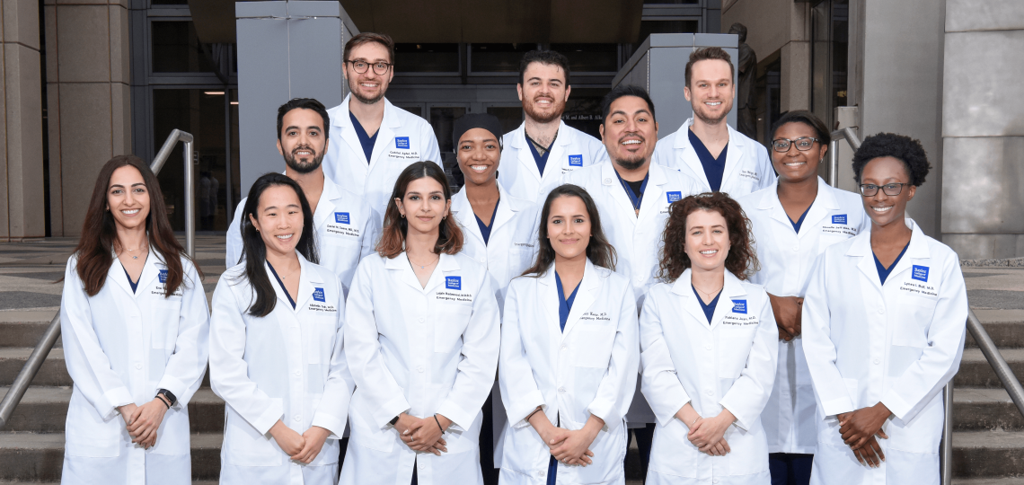 13 residents in white coats stand together