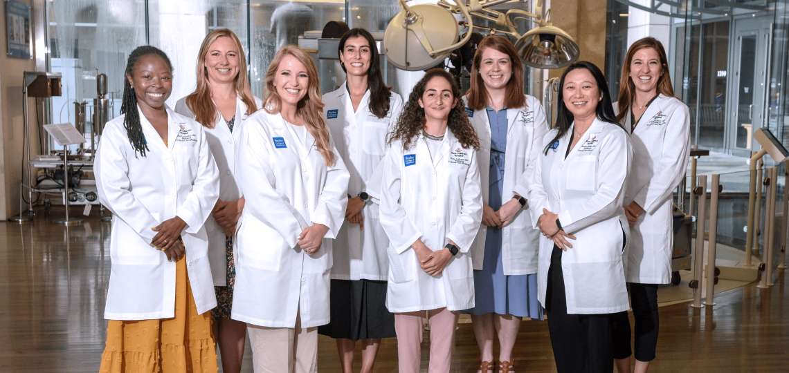 First-year fellows in white coats pose in the DeBakey library