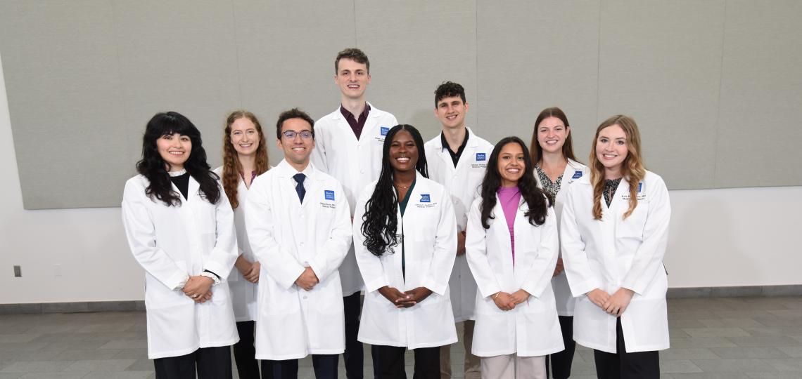 A group of smiling students wearing their white coats.