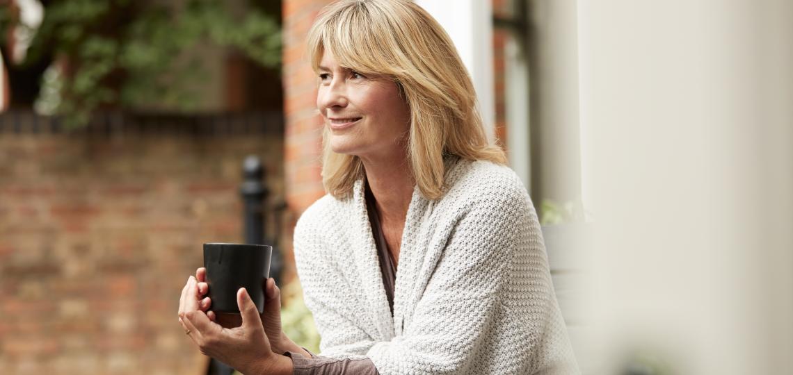 Woman sitting outside, smiling and holding a black mug.