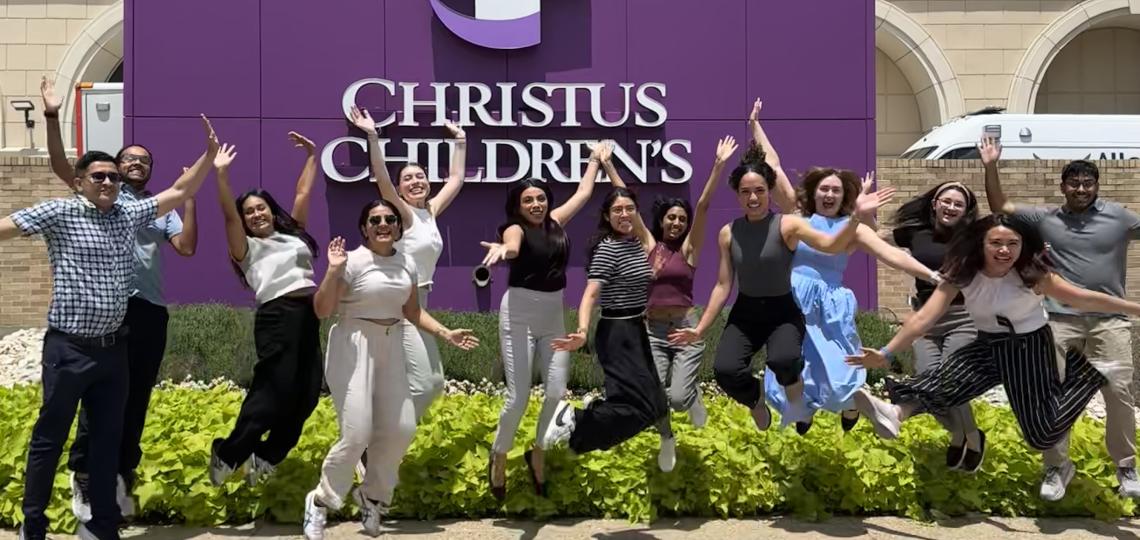 people jumping and smiling in front of a christus children's sign