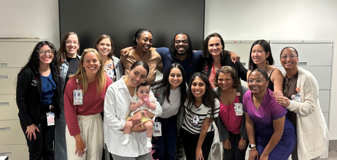 group of people standing together and smiling while one woman holds a baby