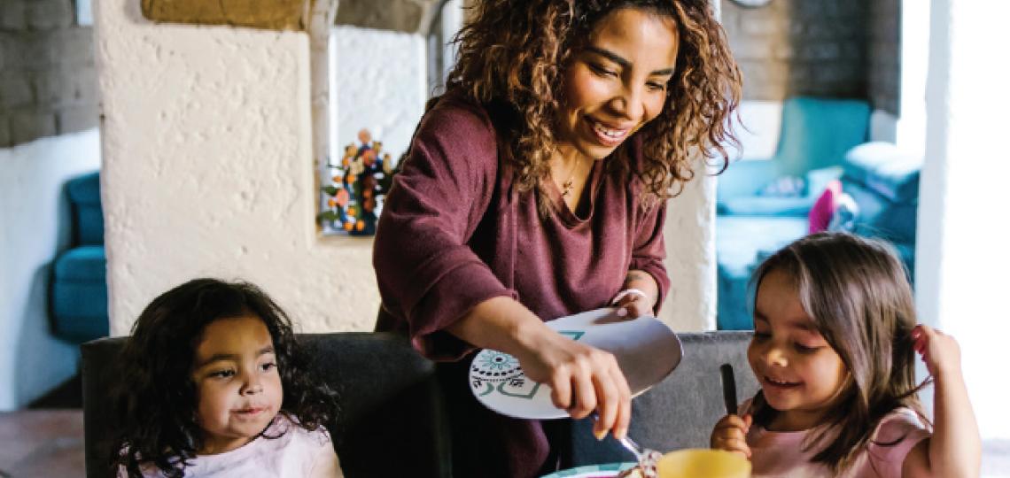 A parent dishing food out onto two children's plates.