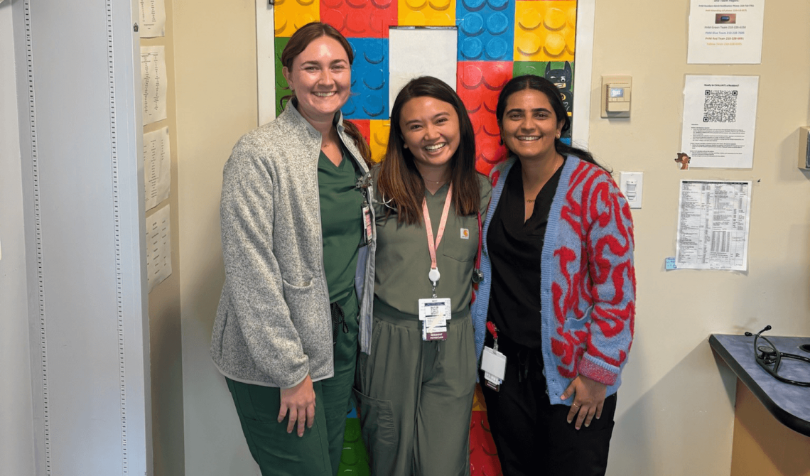Three smiling residents standing in front of a door decorated with a poster of LEGO blocks