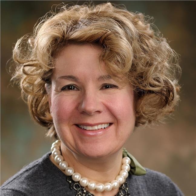 woman with short curly hair and big pearl necklace smiling