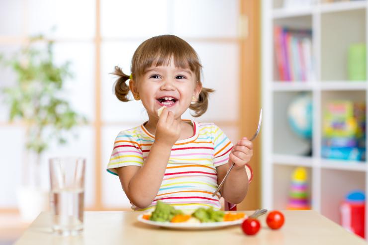 baby girl in pigtails eating plate of vegetables