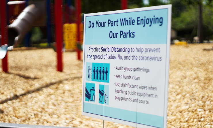 A sign suggesting social distancing posted in front of a playground.