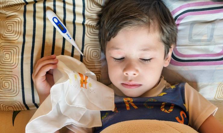 Photo of a little boy in bed with a thermometer and a hankerchief  