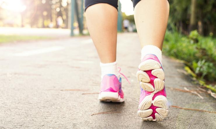 Close up photo of feet wearing tennis shoes, walking on a sidewalk.