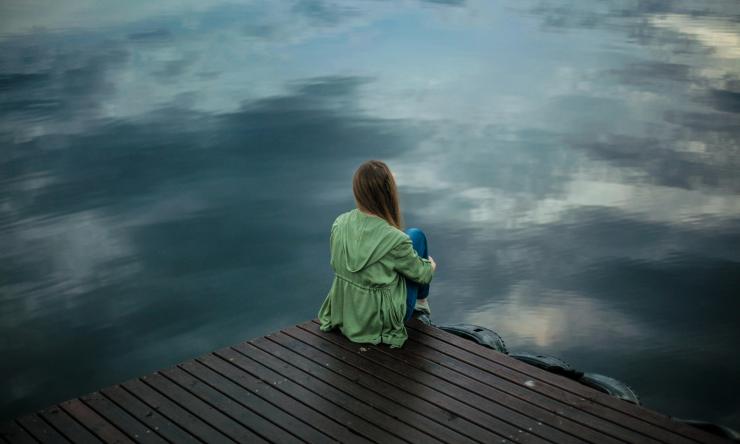 Photo of a woman sitting alone on a dock in the dim fall light. 