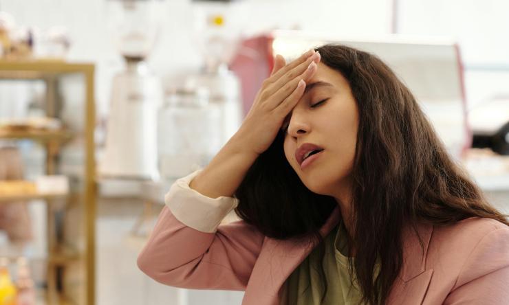 A woman is sitting at work with her hand on her forehead and eyes closed, she is coming down with a cold.
