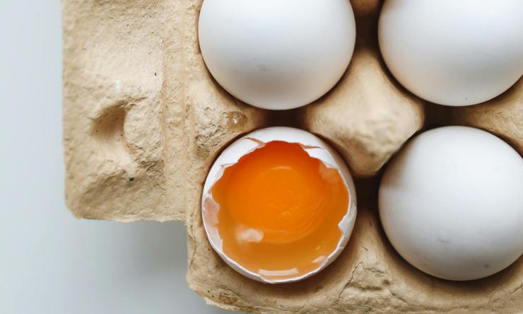 Photo of eggs in an open egg carton with one broken showing the yellow yolk.  