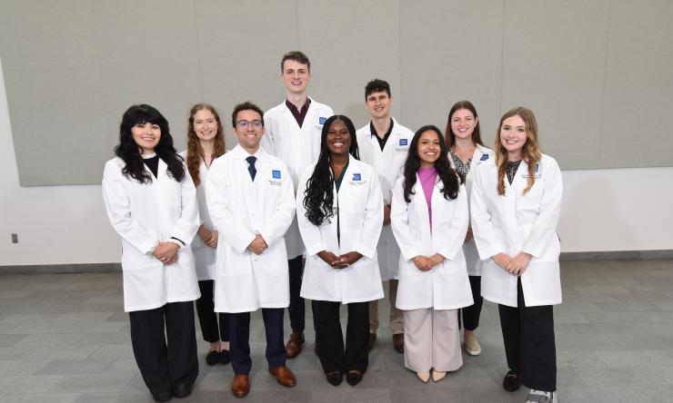 A group of smiling students wearing their white coats.