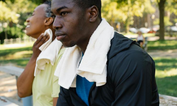 Two men sit outside in the heat, wearing towels around their neck to wipe their sweat. 