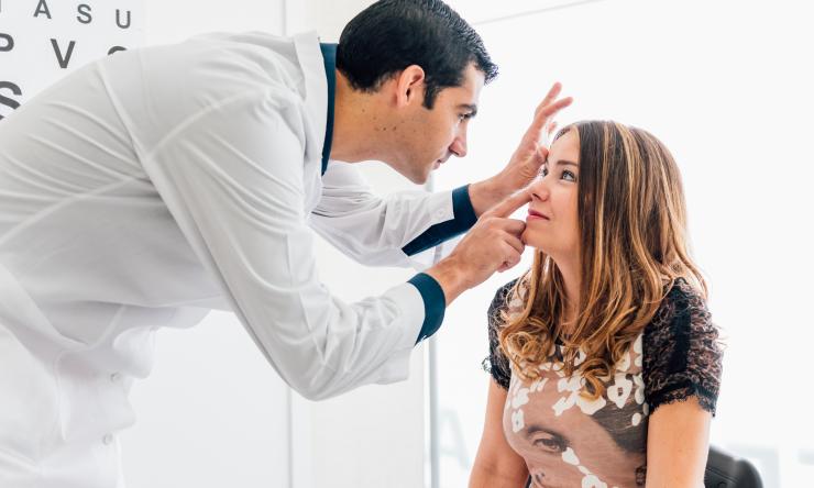 A patient sits while a doctor performs an eye exam.