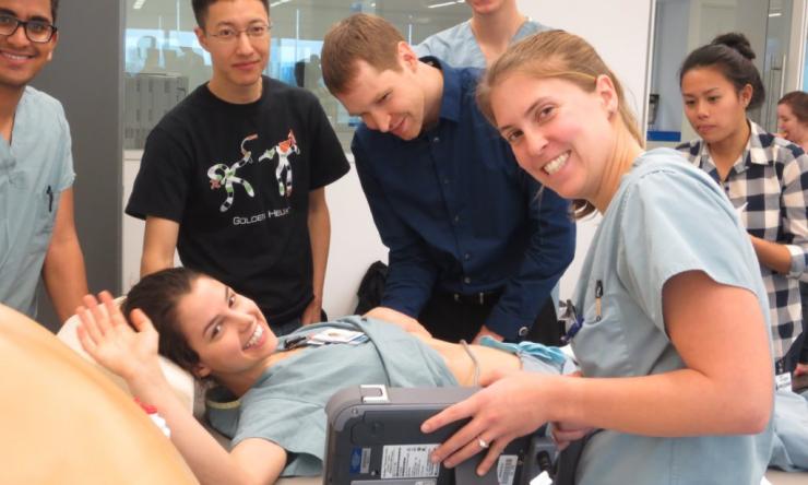 Several smiling students practice medical procedures on a volunteer